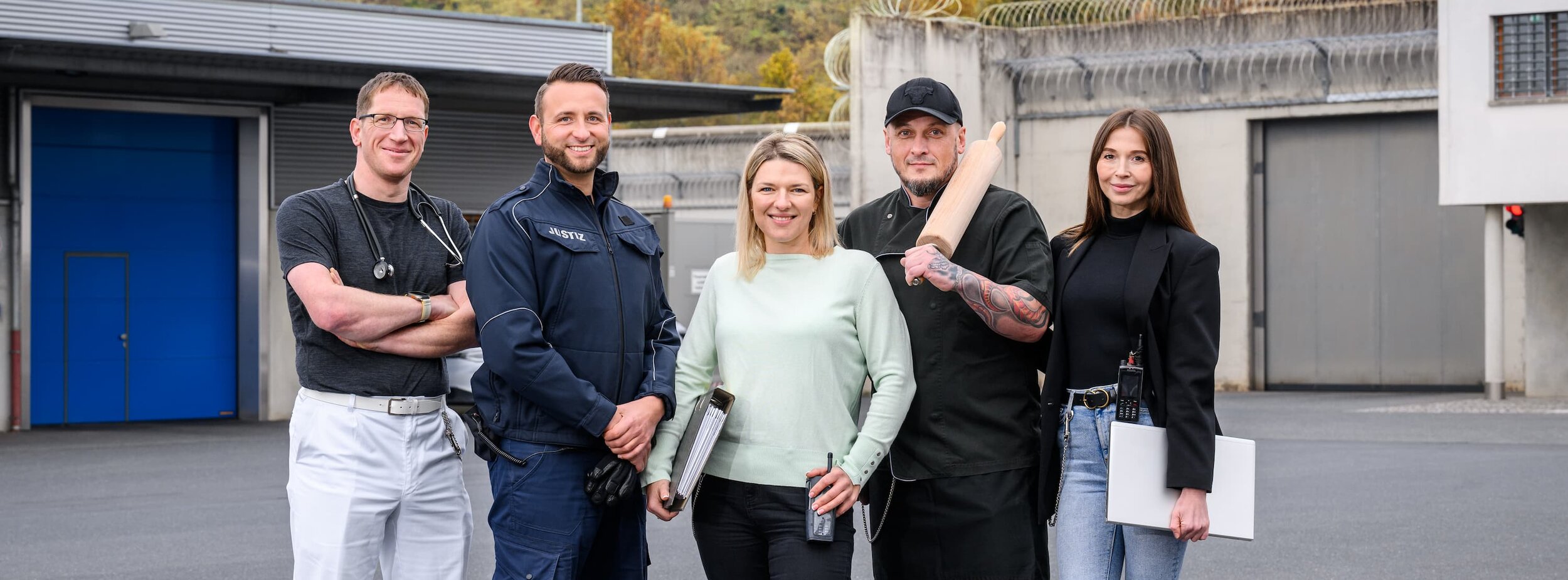 Fünf Mitarbeiter verschiedener Fachgebiete Justizvollzugs stehen auf dem Hof einer Justizvollzugsanstalt