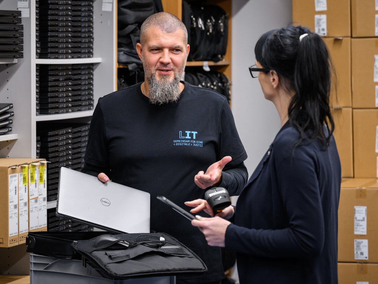 Ein Mitarbeiter und eine Mitarbeiterin der Leitstelle für IT für Beschaffung im Gespräch mit Notebooks im Lager