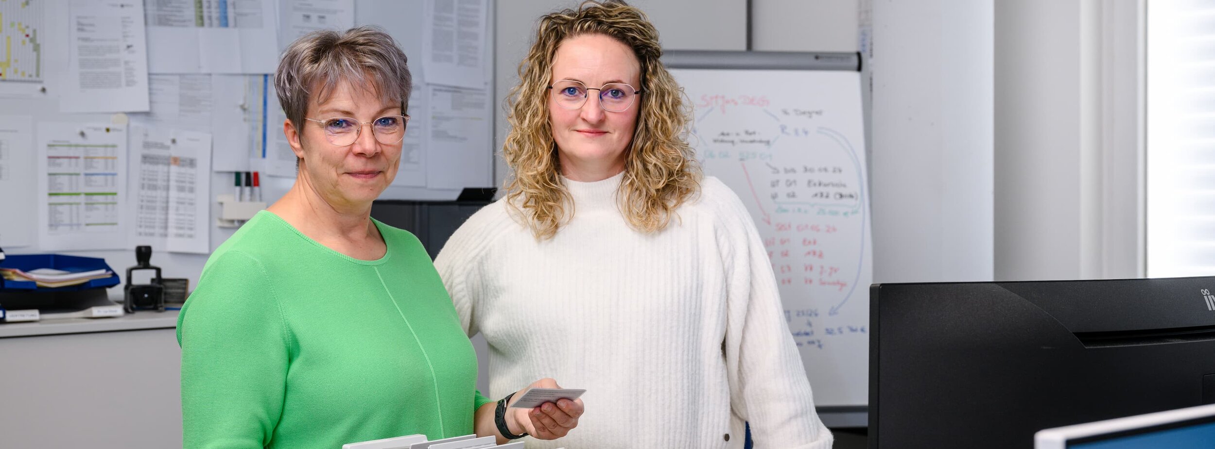 Zwei Sachbearbeiterinnen stehen an einem Schreibtisch