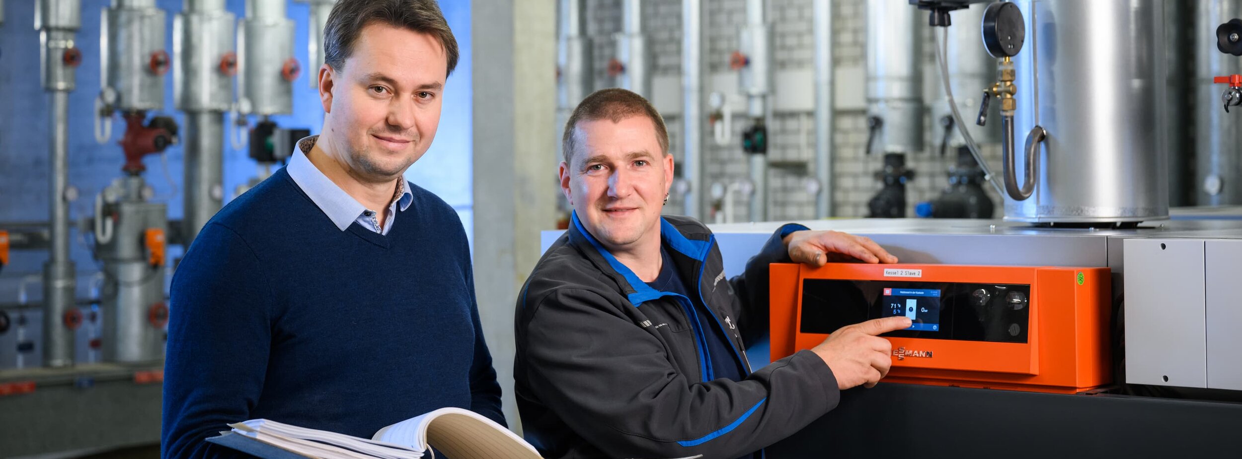 Zwei Hausmeister stehen an einer Heizungsanlage