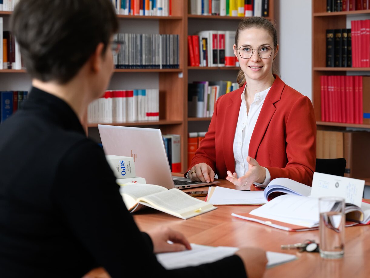 Eine junge Staatsanwältin im Büro beim Studieren der Akten im Gespräch mit einer Kollegin