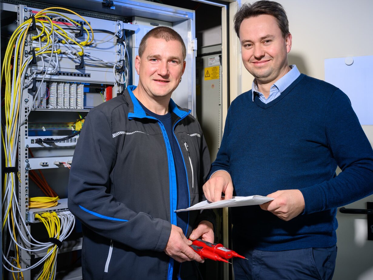 Zwei Hausmeister stehen vor einem geöffneten Schaltschrank