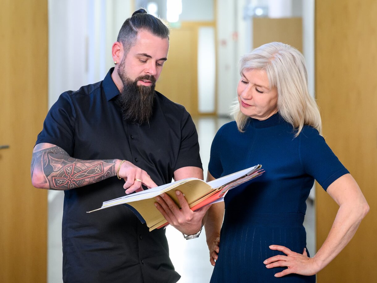 Ein Justizfachwirt und eine Justizfachwirtin im Gespräch; der Justizfachwirt zeigt etwas in einer Akte