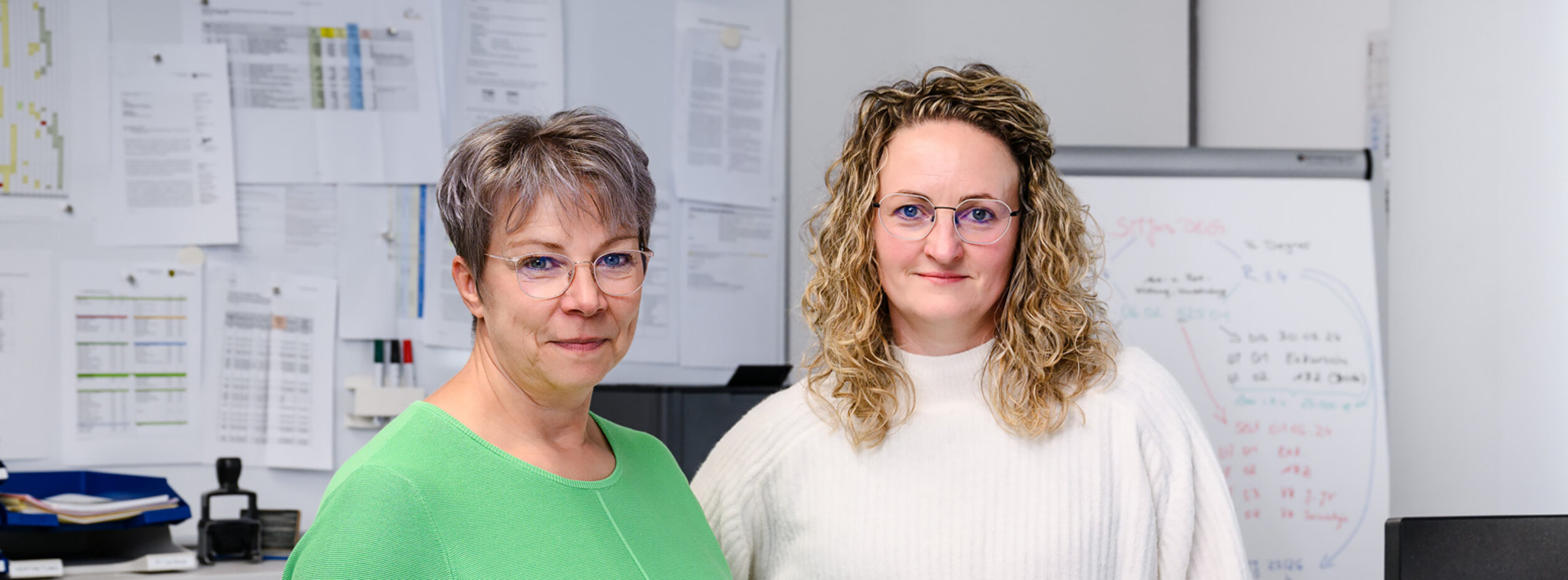 Zwei Sachbearbeiterinnen stehen an einem Schreibtisch
