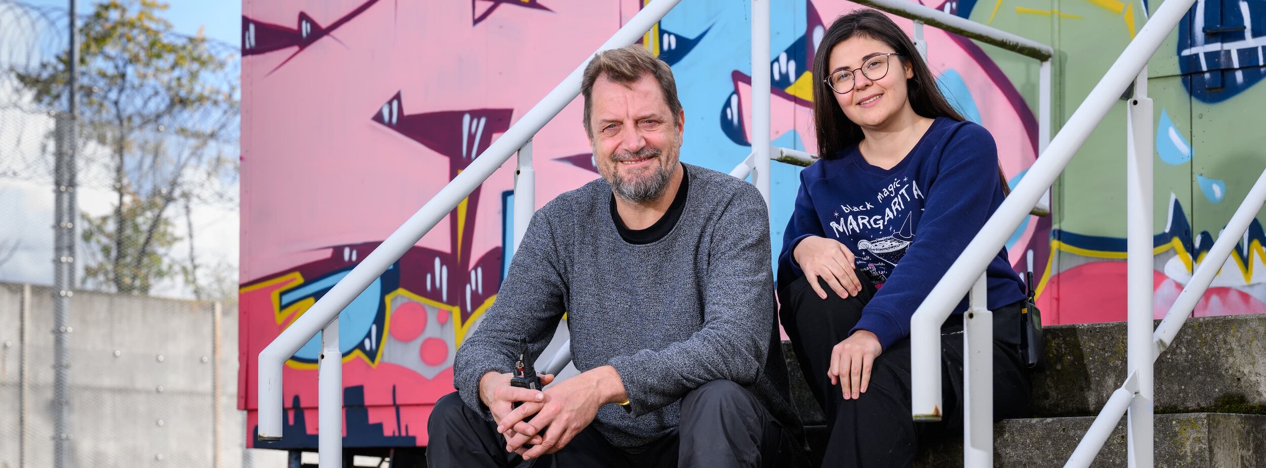Ein Mitarbeiter und eine Mitarbeiterin sitzen auf der Treppe vor dem Kreativzentrum im Justizvollzug