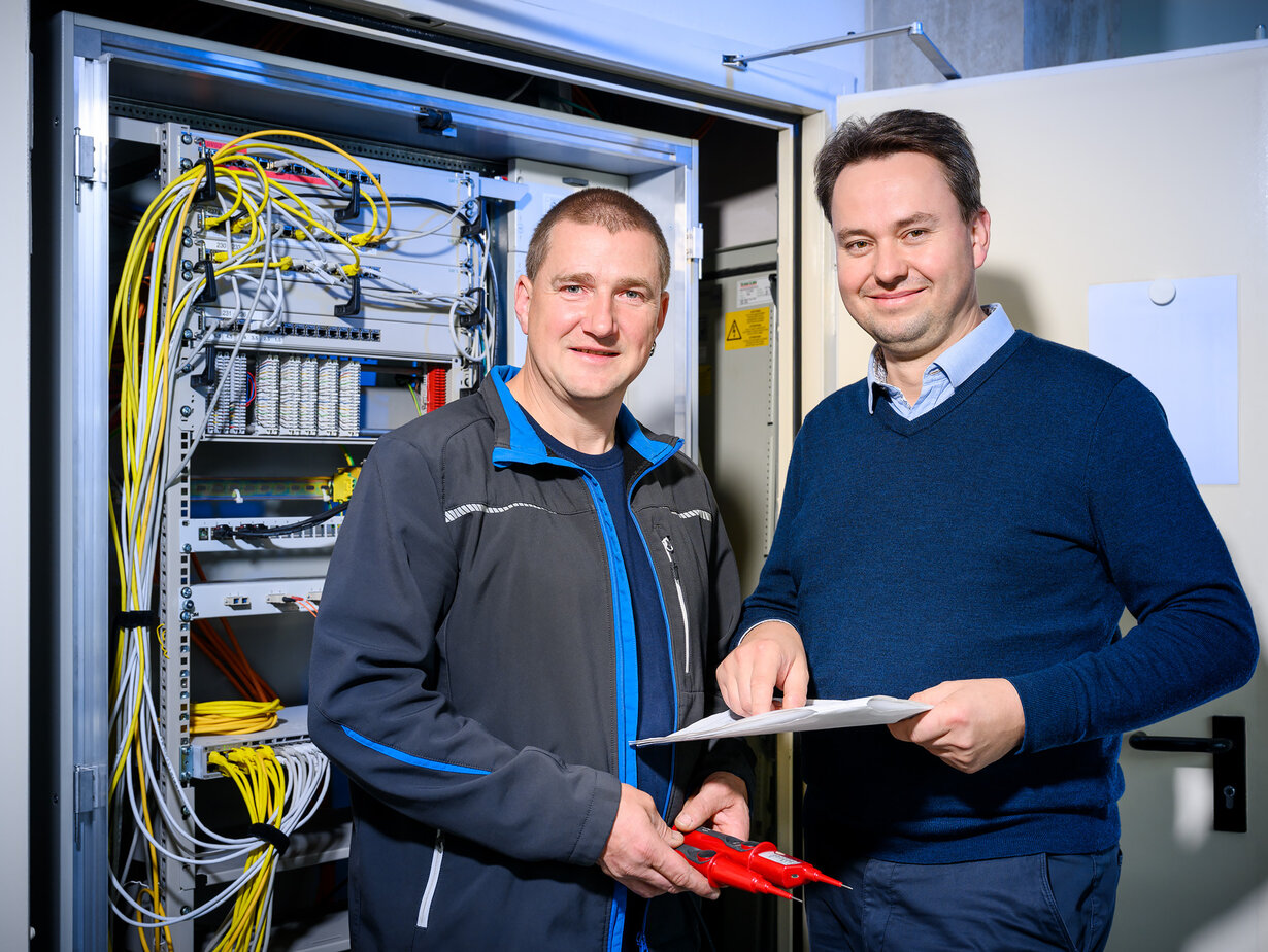 Zwei Hausmeister stehen vor einem geöffneten Schaltschrank