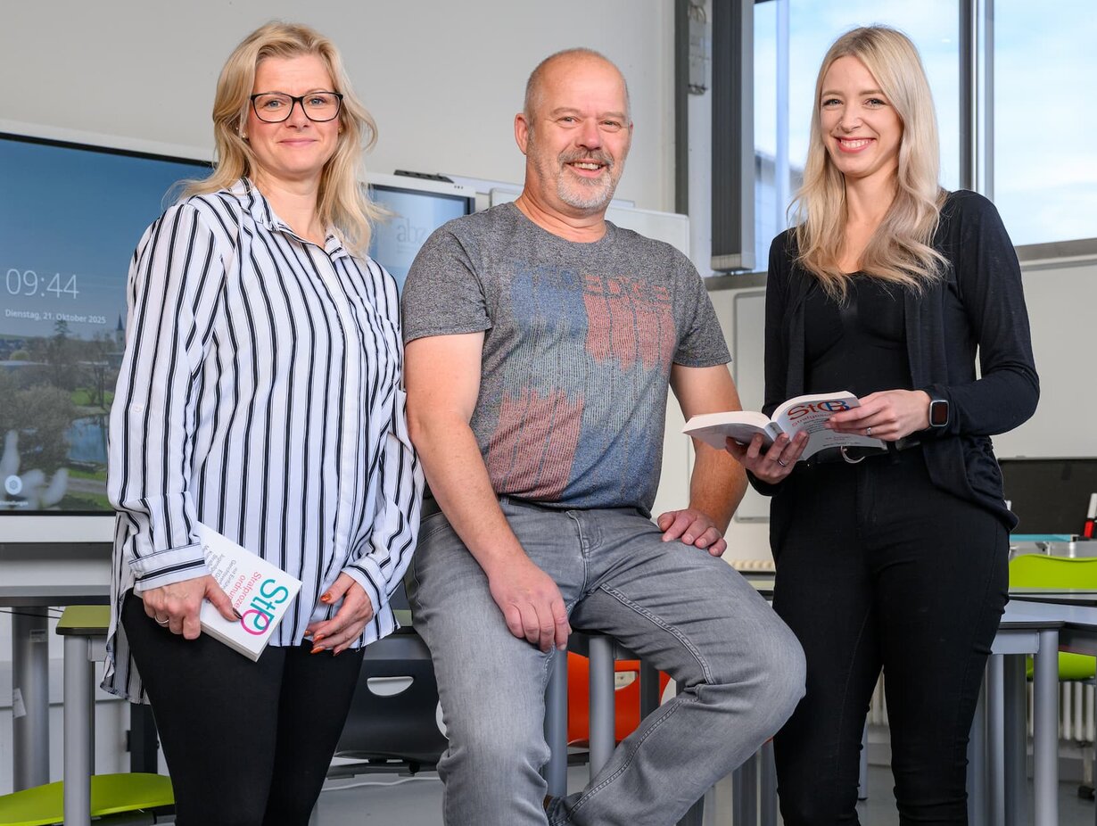 Drei Lehrkräfte in einem Klassenzimmer, 1 Mann in der Mitte und links und rechts eine Frau