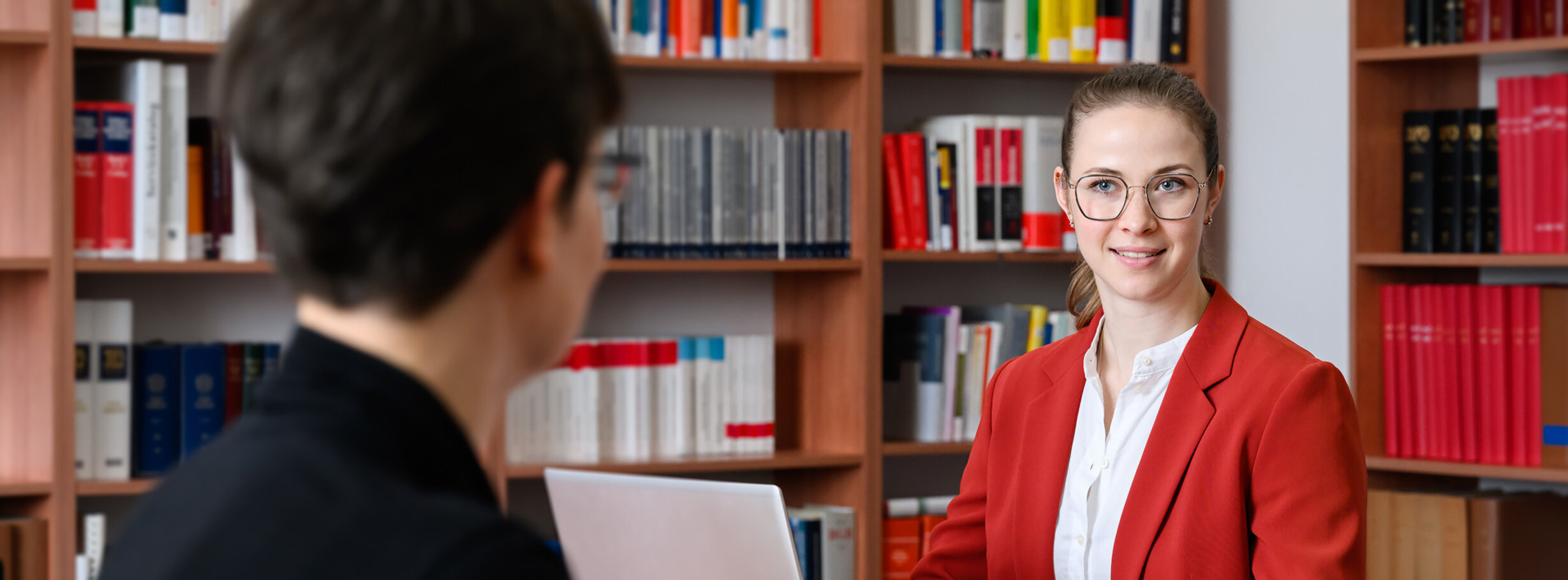 Eine junge Staatsanwältin im Büro beim Studieren der Akten im Gespräch mit einer Kollegin