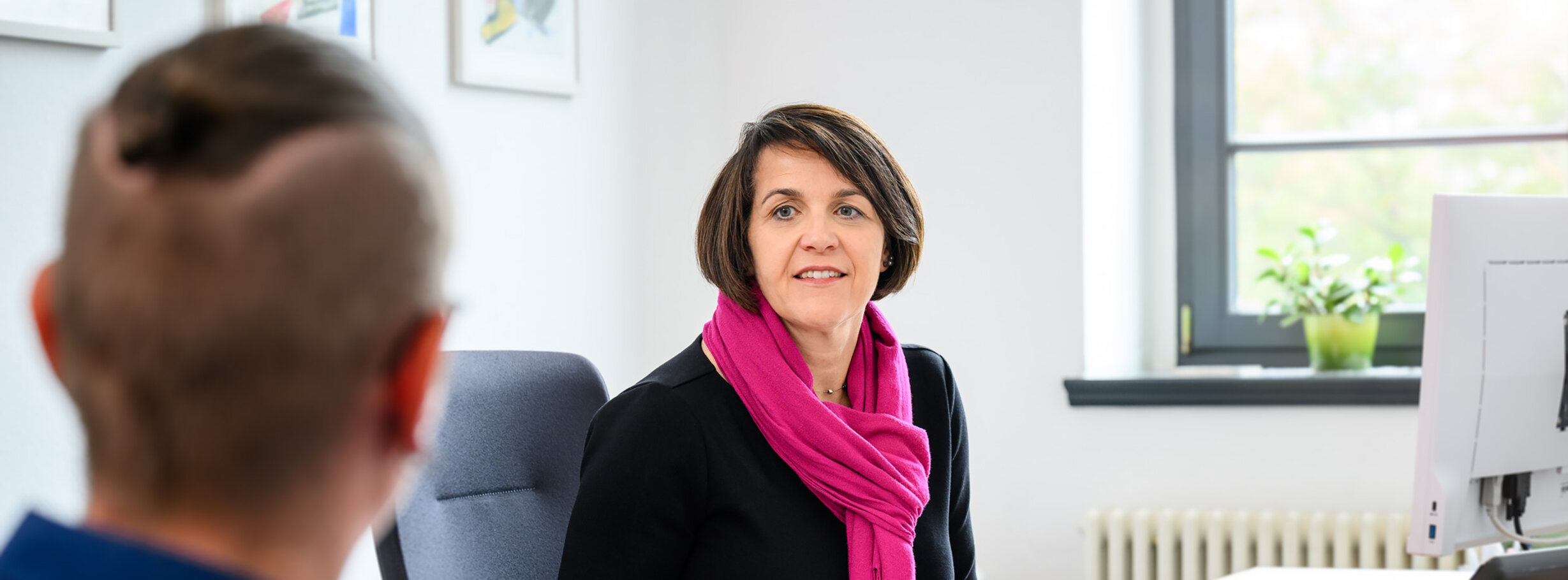 Eine Amtsanwältin an ihrem Schreibtisch spricht mit einer Person