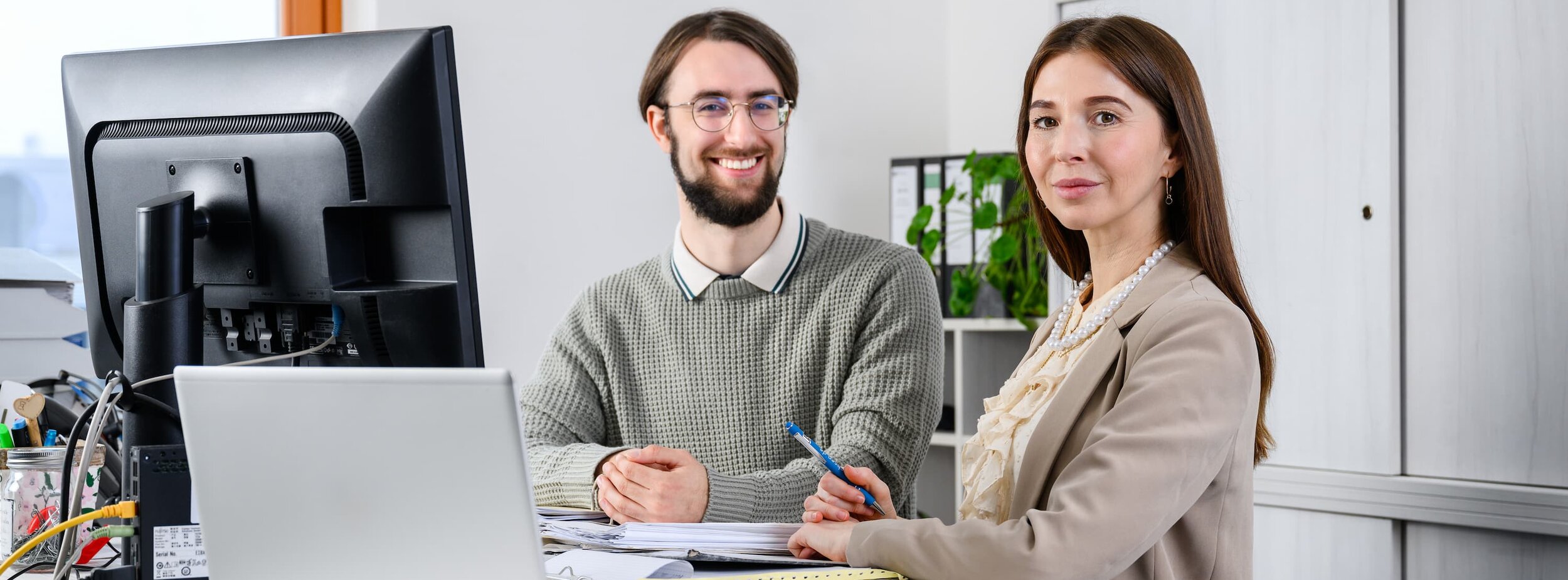 Ein Mitarbeiter und eine Mitarbeiter des Verwaltungsdienstes im Justizvollzug an einem Schreibtisch