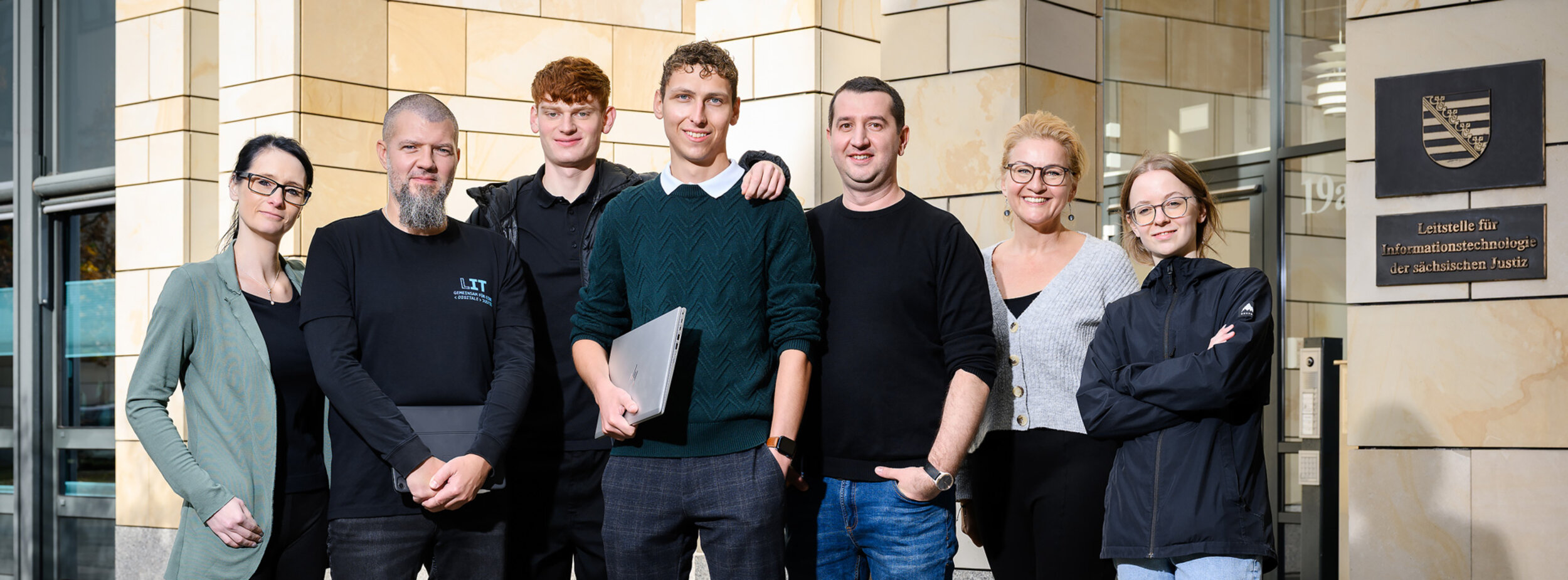 Eine Gruppe von Mitarbeitern verschiedener Fachgebiete der Leitstelle für IT stehen vor einem Gebäude