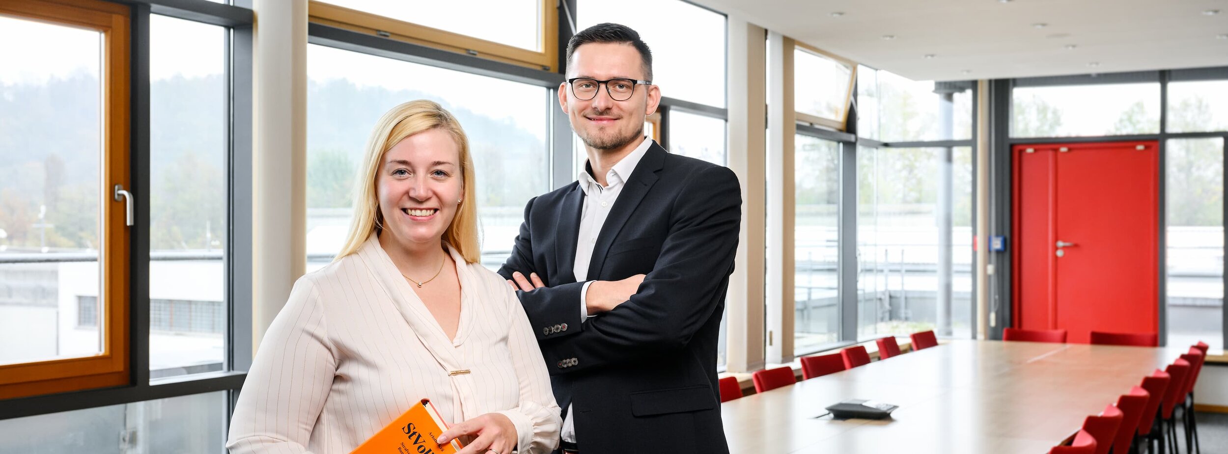 Eine Juristin und ein Jurist stehen in einem Raum des Justizvollzuges; die Juristin hält ein Buch unter dem Arm