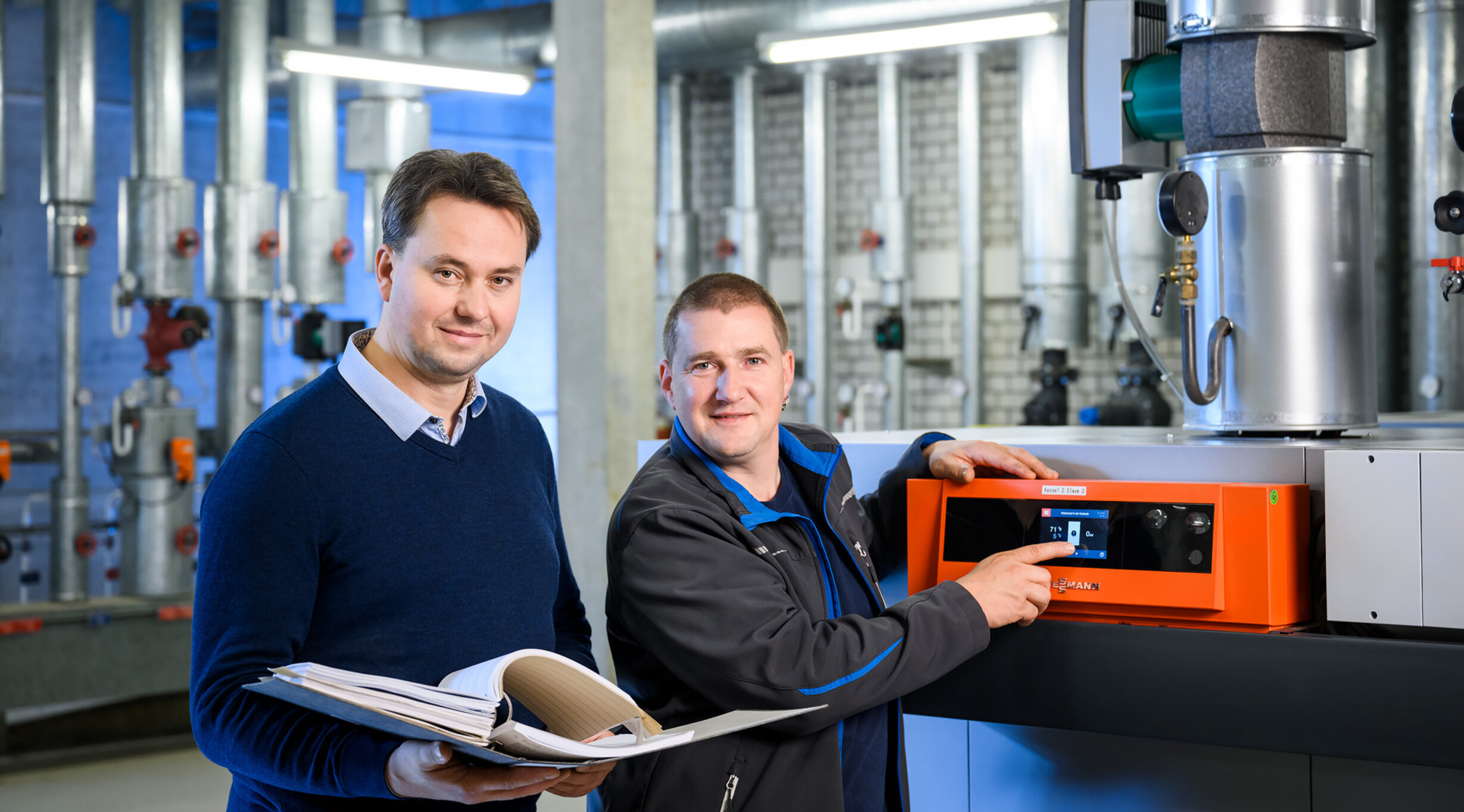 Zwei Hausmeister stehen an einer Heizungsanlage